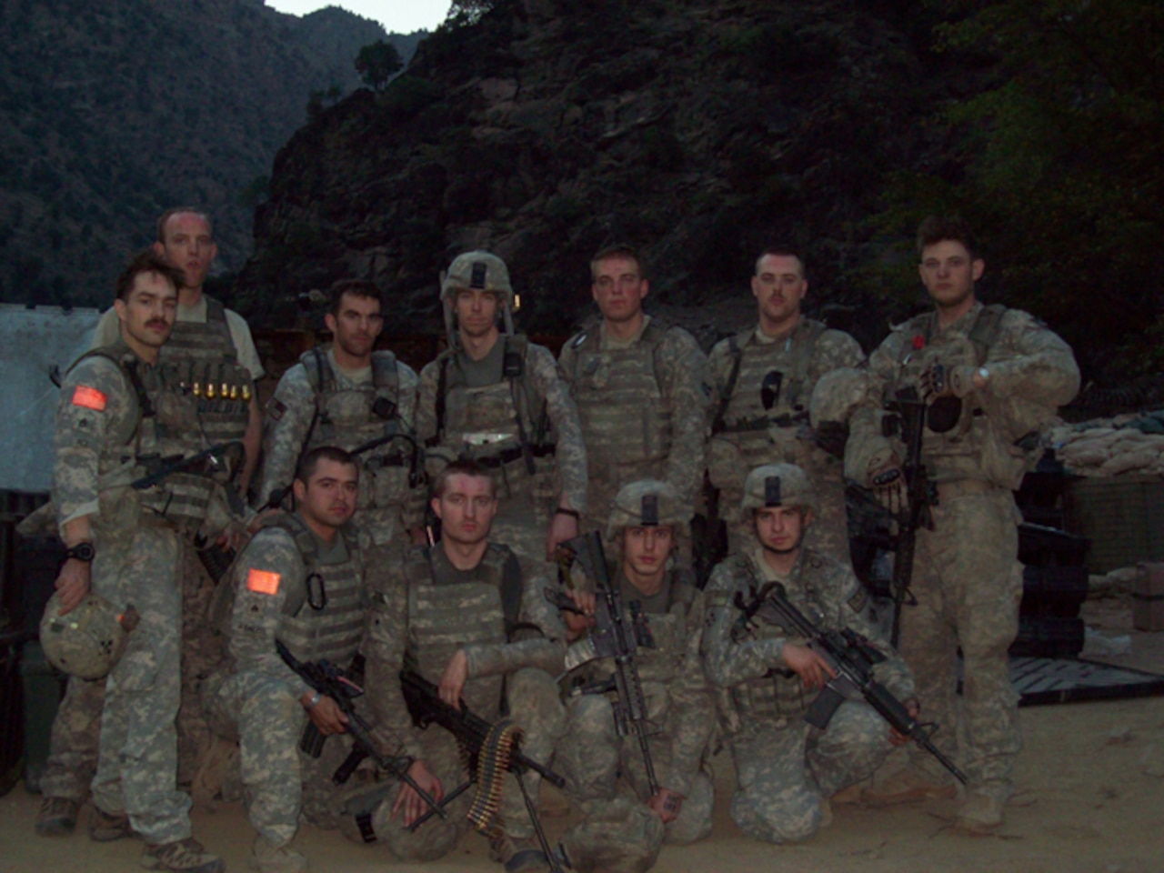 Eleven men in combat uniforms and rifles pose for a photo.
