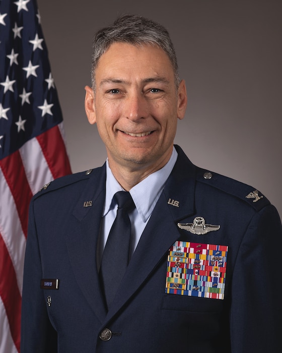 An Air Force Colonel smiles in front of an American flag