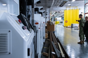 Two men stand inside a warehouse looking at a line of automated, robotic vehicles