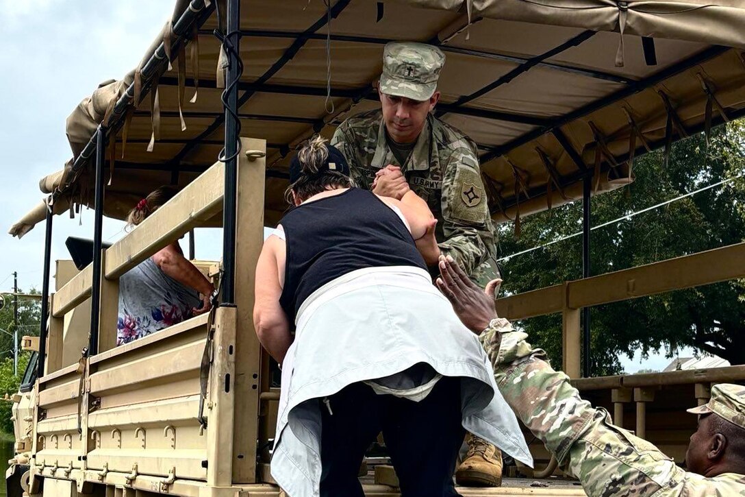 Two soldiers help a civilian climb up and into the open back of a military vehicle.