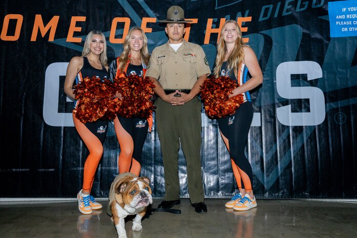 U.S. Marine Corps Staff Sgt. Karlo Esquivel, training chief and the voice with Recruit Training Regiment, and Lance Cpl. Bruno, the mascot for Marine Corps Recruit Depot San Diego and the Western Recruiting Region, pose for a picture at a San Diego Gulls event at Pechanga Arena San Diego, California, Oct. 5, 2024. The Marines attended the event to help build community relations and give a shout out for MCRD San Diego’s upcoming event, the Boot Camp Challenge, which will take place on Oct. 19, 2024. (U.S. Marine Corps photo by Lance Cpl. Janell B. Alvarez)