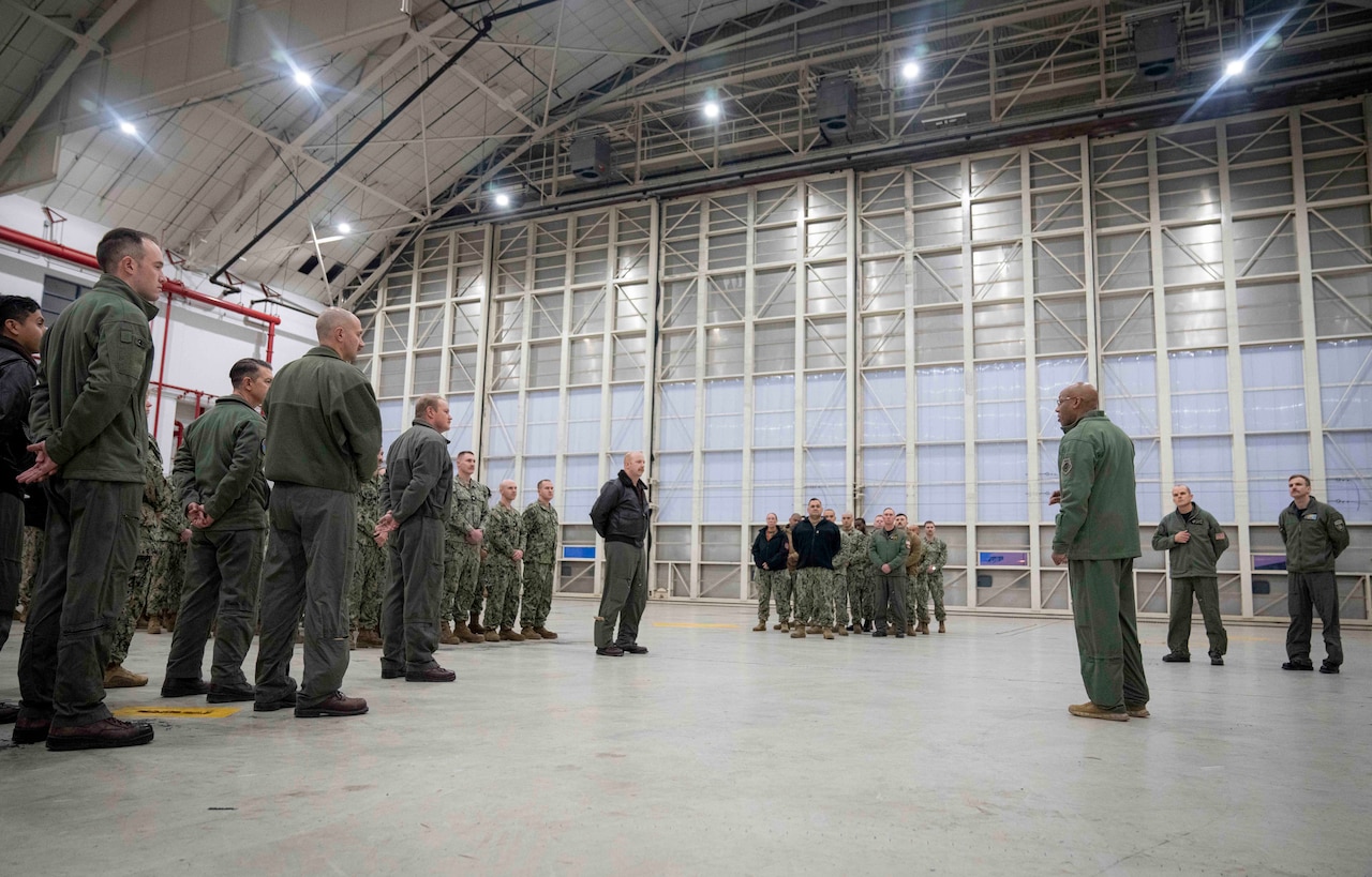 Service members in uniform stand in formation as an officer speaks to them.