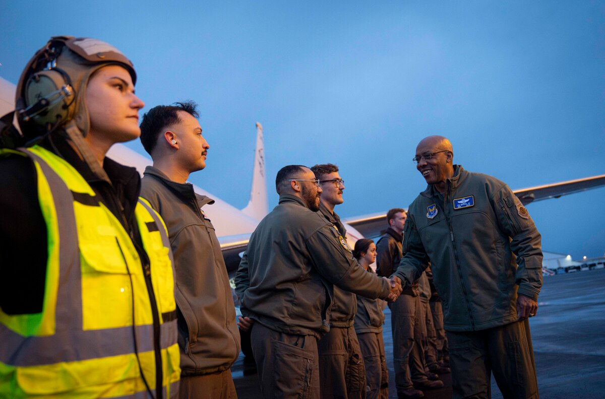 A service member in flight gear shakes hands with service members near an aircraft.