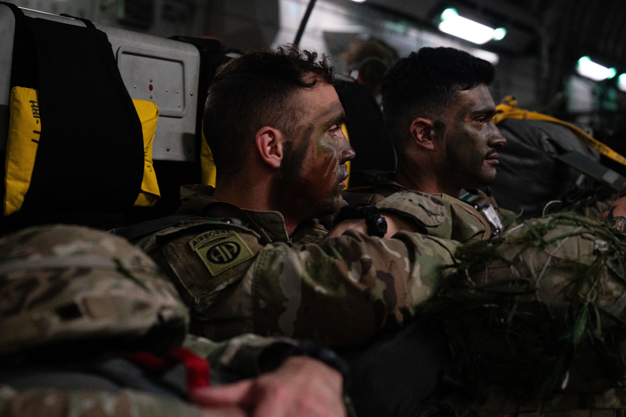 U.S. Army Soldiers with camouflage face paint sits inside a C-17 Globemaster III aircraft.
