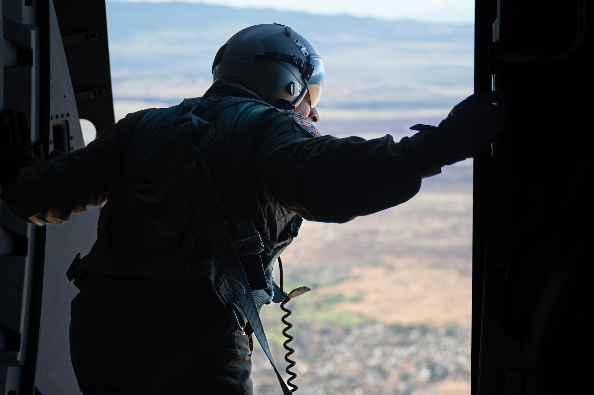 A U.S. Air Force loadmaster looks outside of an open door on a C-17 Globemaster III aircraft midflight.