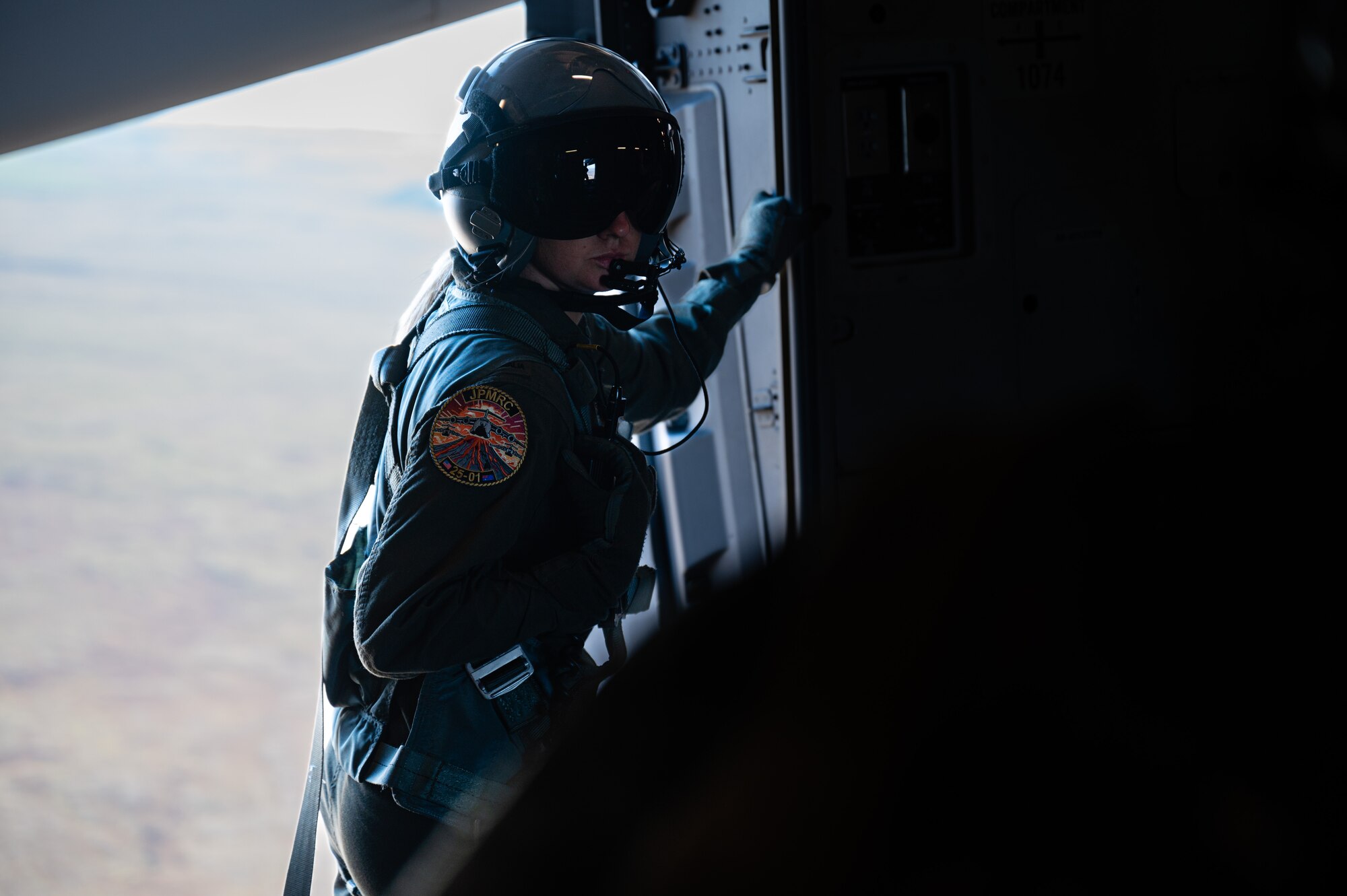 Royal Australian Air Force loadmaster stands next to an open door of a C-17 Globemaster III aircraft midflight.
