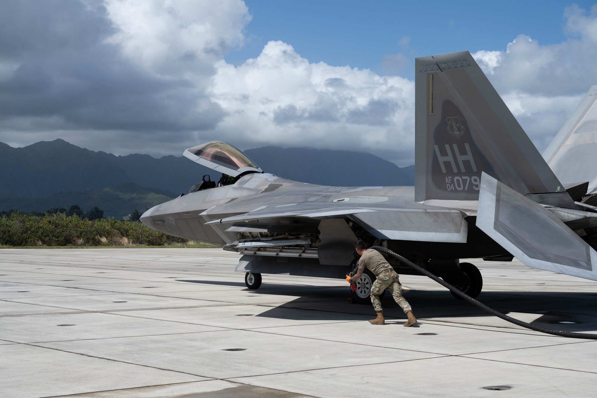 A U.S. Airman pulls a fuel pump over his shoulder to a F-22 Raptor Aircraft.
