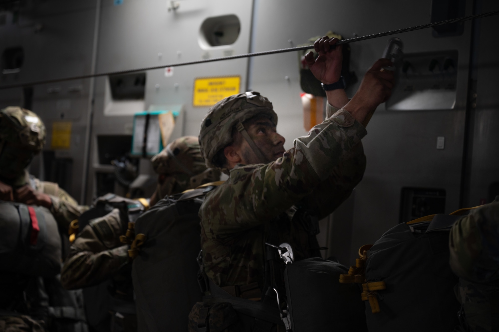 A U.S. Army Soldier assigned to the 11th Airborne Division hooks his parachute to a static line during Joint Pacific Multinational Readiness Center 25-01 over Hilo, Hawaii, Oct. 7, 2024. The Joint Pacific Multinational Readiness Center (JPMRC) is the Army’s newest Combat Training Center (CTC) and generates readiness in the environments and conditions where our forces are most likely to operate in. JPMRC 25-01 highlights our commitment to partnership and a free and open Indo-Pacific and includes training participants from across the U.S. Joint Force and multinational Allies and partners. (U.S. Air Force photo by Senior Airman Mark Sulaica)