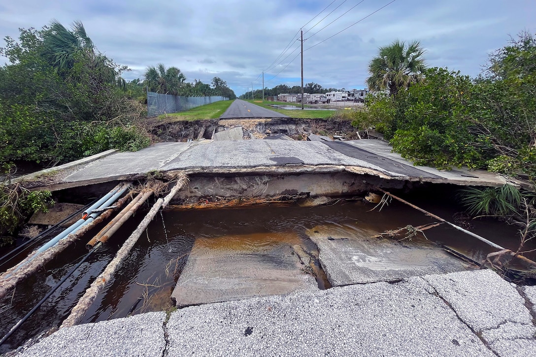 A large chunk of a road is collapsed on its entire width during an overcast day.