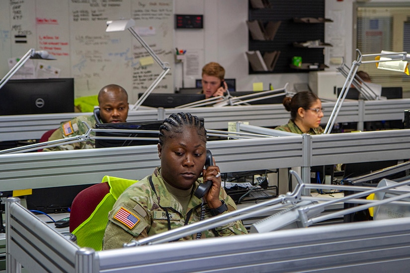 Soldiers take phone calls seated at desks in an office setting.