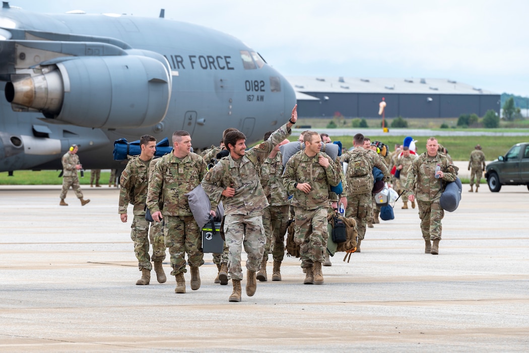 a group of airmen carrying bags walk across a flight line