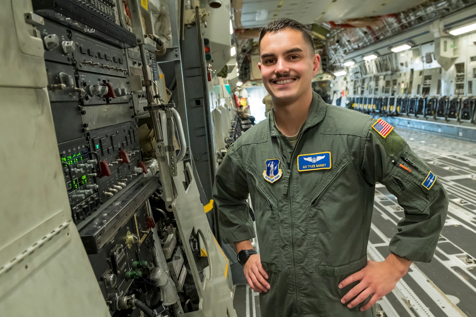 a man in unform stands next to a control panel in the cargo area of an aircraft