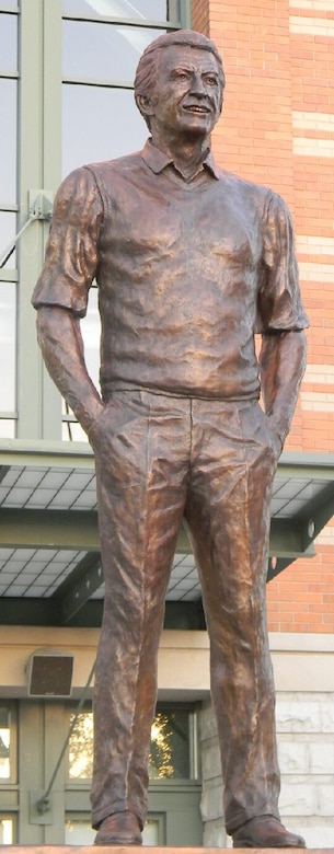 A large statue of a person whose hands are in their pockets is in front of a building.