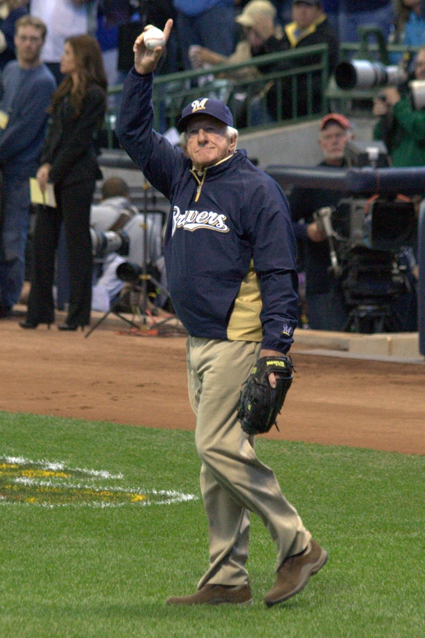 A person holding a baseball and standing on a baseball field raises their arm.