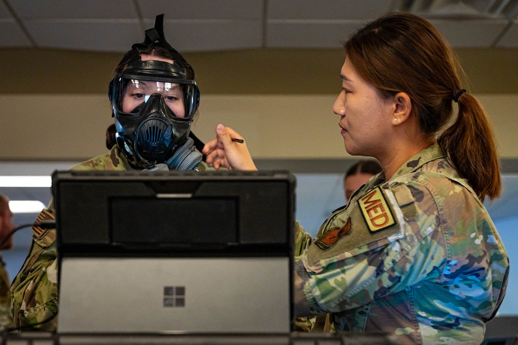 U.S. Air Force Airman 1st Class Olivia Huston (left), 56th Security Forces Squadron installation entry controller, is fitted with a gas mask by Airman 1st Class Minah Hong (right), 56th Medical Group bioenvironmental engineer specialist.