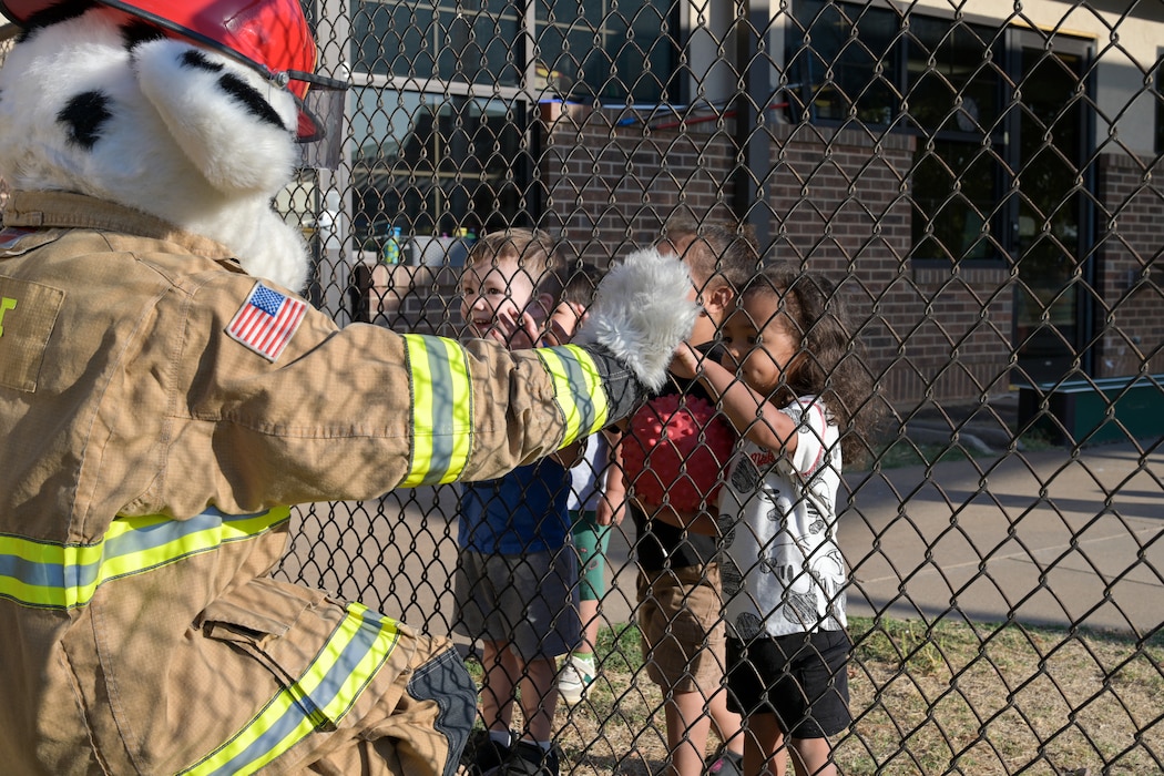 Sparky, the Fire Prevention Week mascot, greets children at the Child Development Center (CDC) at Altus Air Force Base, Oklahoma, Oct. 8, 2024. The 97th Civil Engineer Squadron fire team walked around the CDC and brought a fire truck to show the children in the spirit of Fire Prevention Week. (U.S. Air Force photo by Airman 1st Class Lauren Torres)