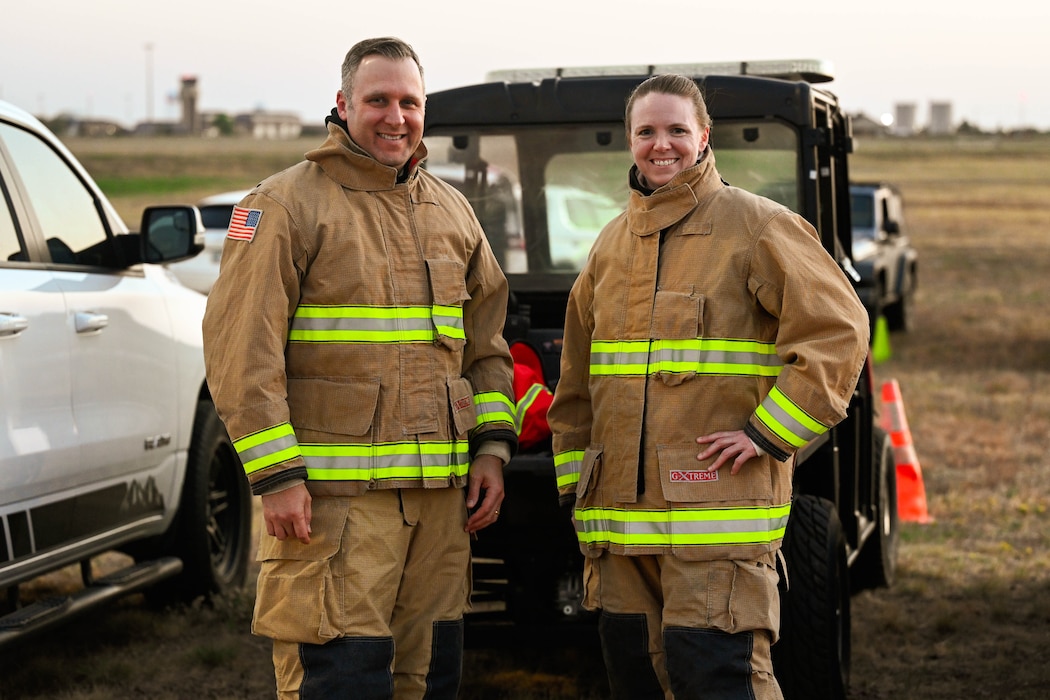 U.S. Air Force Col. Amanda Knotts, 97th Mission Support Group (MSG) commander, and Chief Master Sgt. Andrew Shone, MSG command chief, pose for a photo in personal protective equipment before participating in a live fire exposition for fire prevention week at Altus Air Force Base (AFB), Oklahoma, Oct. 9, 2024. The 97th Civil Engineer Squadron firefighters allowed their group command team to fight a controlled aircraft fire during the event. (U.S. Air Force photo by Airman 1st Class Jonah Bliss)