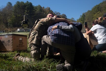 U.S. Army Sgt. Isaac Bradshaw, a combat medic with C Company, 230th Brigade Support Battalion, North Carolina Army National Guard, wraps his arms around an older couple and uses his body to block them from debris and strong winds produced by the rotorwash of a landing CH-47 Chinook helicopter in Burnsville, North Carolina, Oct. 10, 2024. The Chinook crew brought generators, fuel and other supplies to the remote area after floodwaters washed away the main road after Hurricane Helene.