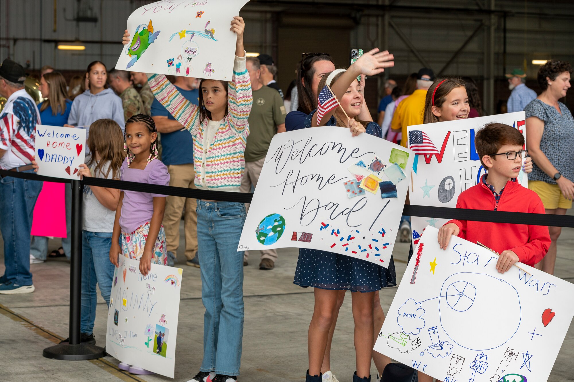 Six children wave and hold welcome home signs