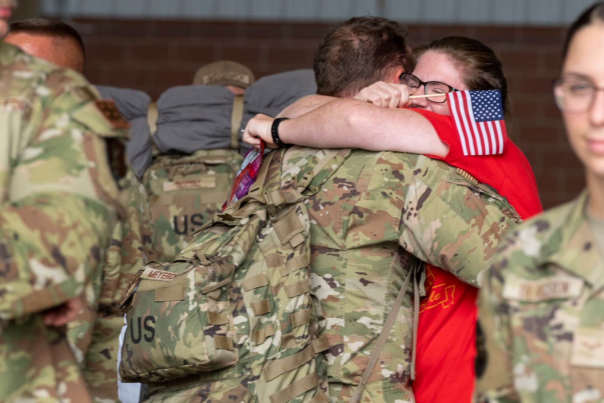 a women holding a small American flag hugs a man in uniform