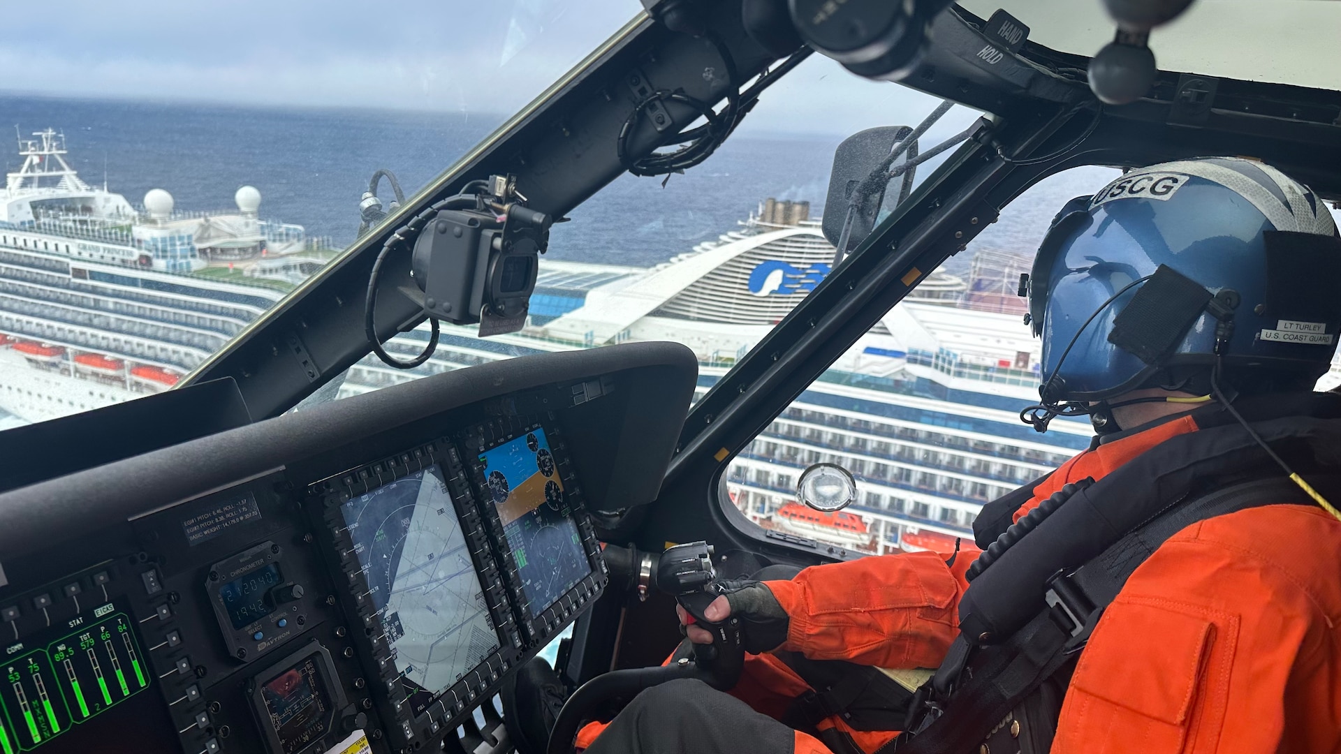 A Coast Guard MH-60 Jayhawk helicopter pilot looks out a cockpit window down at a cruise ship in the ocean.