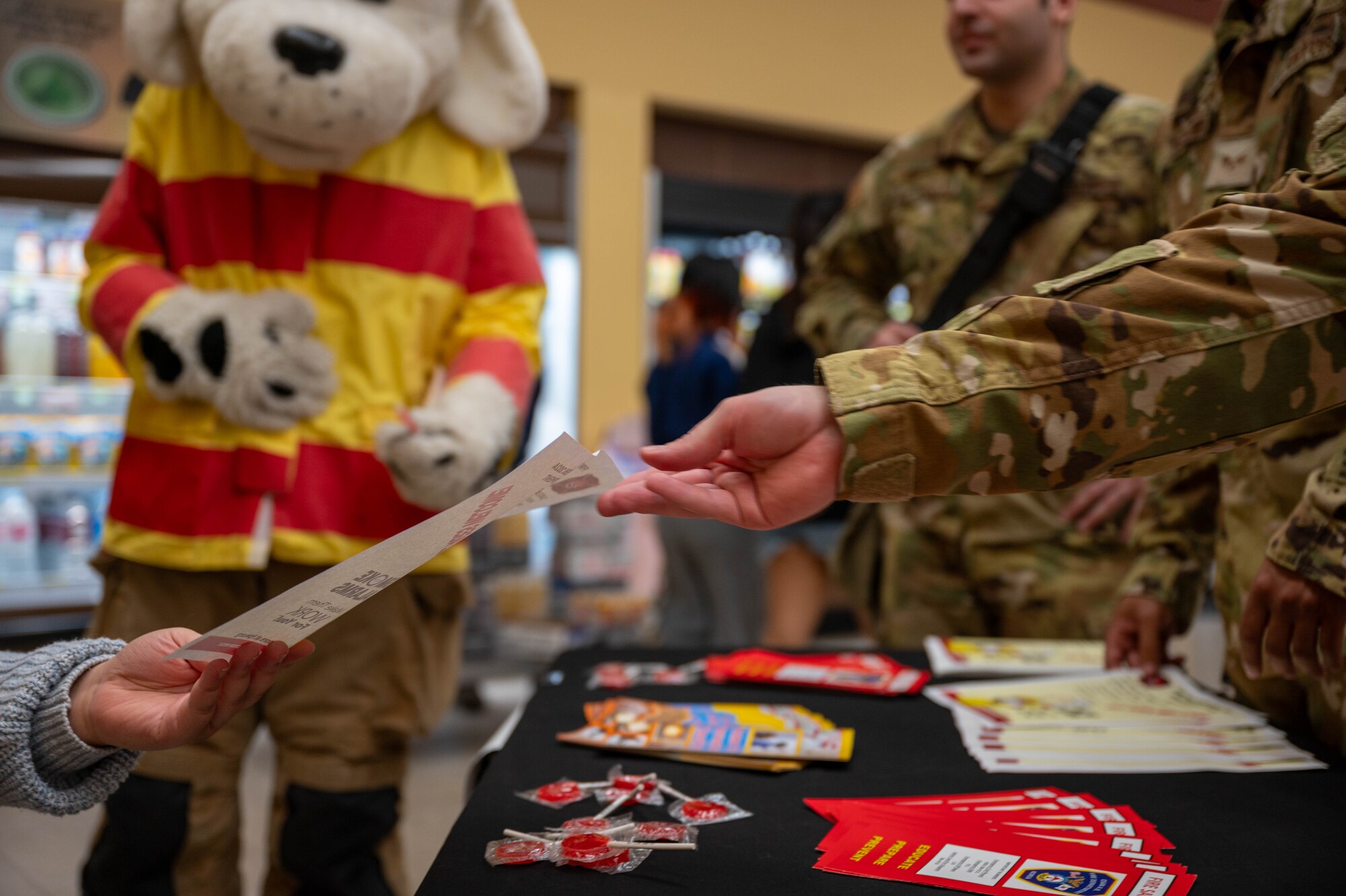 A U.S. Air Force firefighter assigned to the 51st Civil Engineer Squadron, hands a fire prevention flyer to a commissary customer as part of Fire Prevention Week at Osan Air Base, Republic of Korea, Oct. 7, 2024. Fire Prevention Week enhances communication with community members to minimize potential risks during emergencies. (U.S. Air Force photo by Staff Sgt. Christopher Tam)