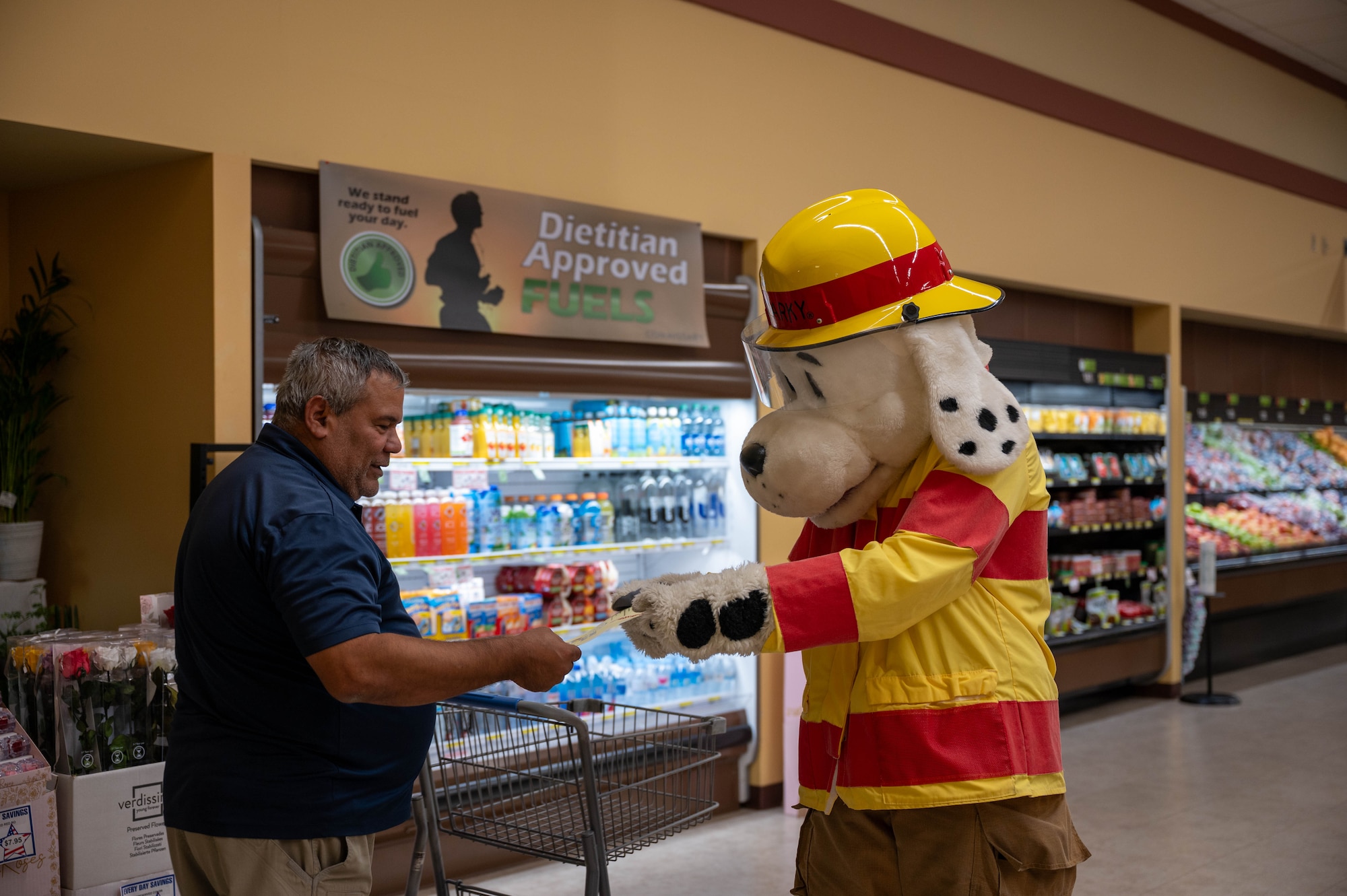 Sparky, National Fire Protection Association mascot, hands a fire prevention flyer to a commissary customer as part of Fire Prevention Week at Osan Air Base, Republic of Korea, Oct. 7, 2024. Sparky and firefighters assigned to the 51st Civil Engineer Squadron set up information booths with fire safety materials at different locations around the base. (U.S. Air Force photo by Staff Sgt. Christopher Tam)