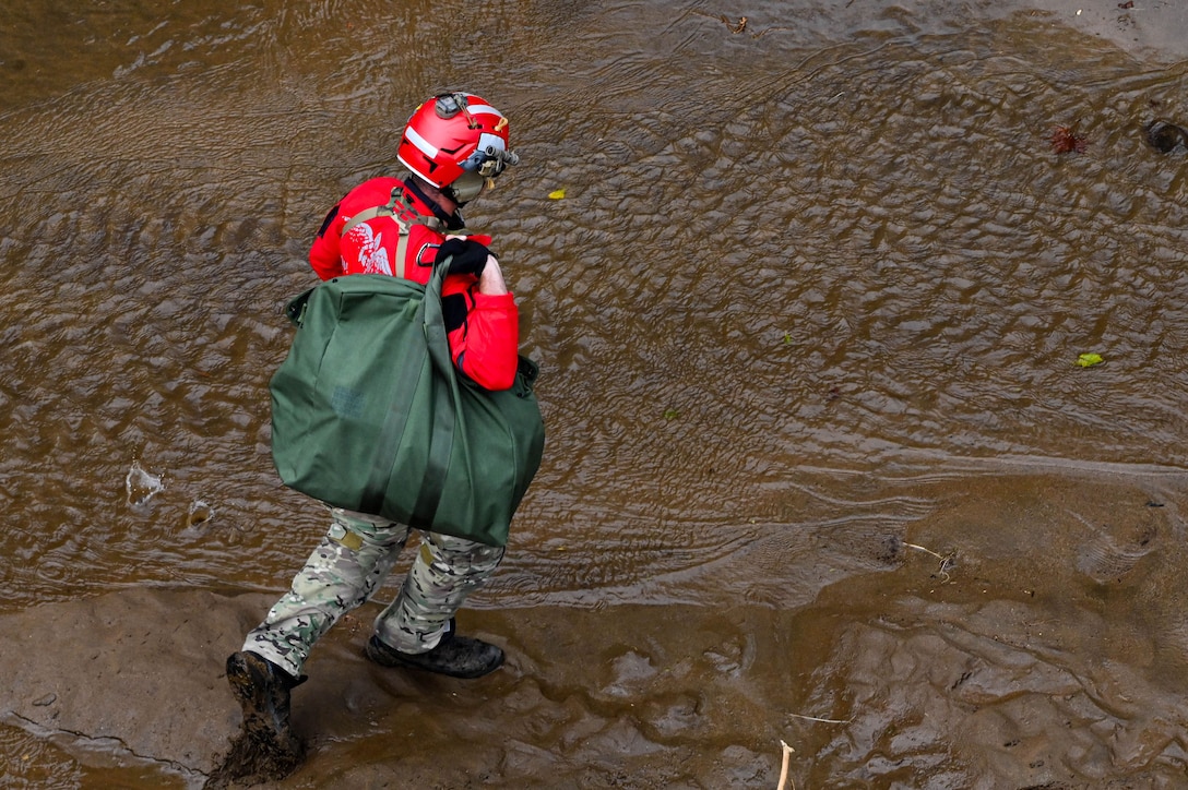 Overhead view of an airman wearing a helmet, carrying a duffel bag while walking in mud.