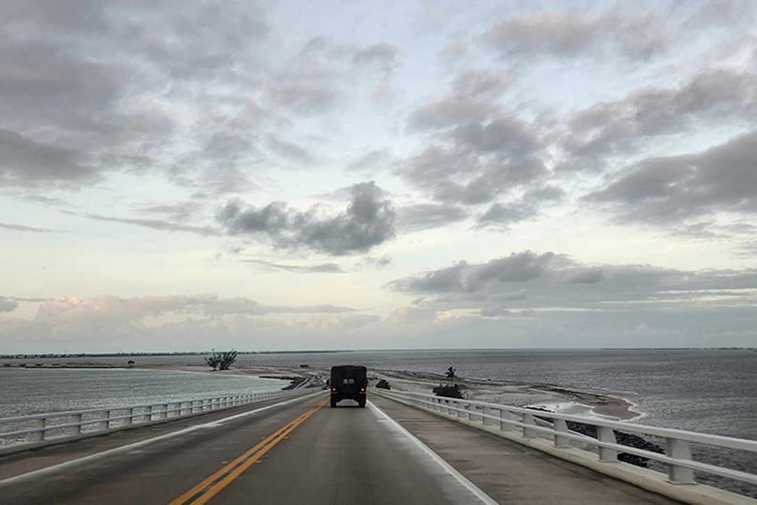 Rear view of a military vehicle driving on a causeway during twilight.