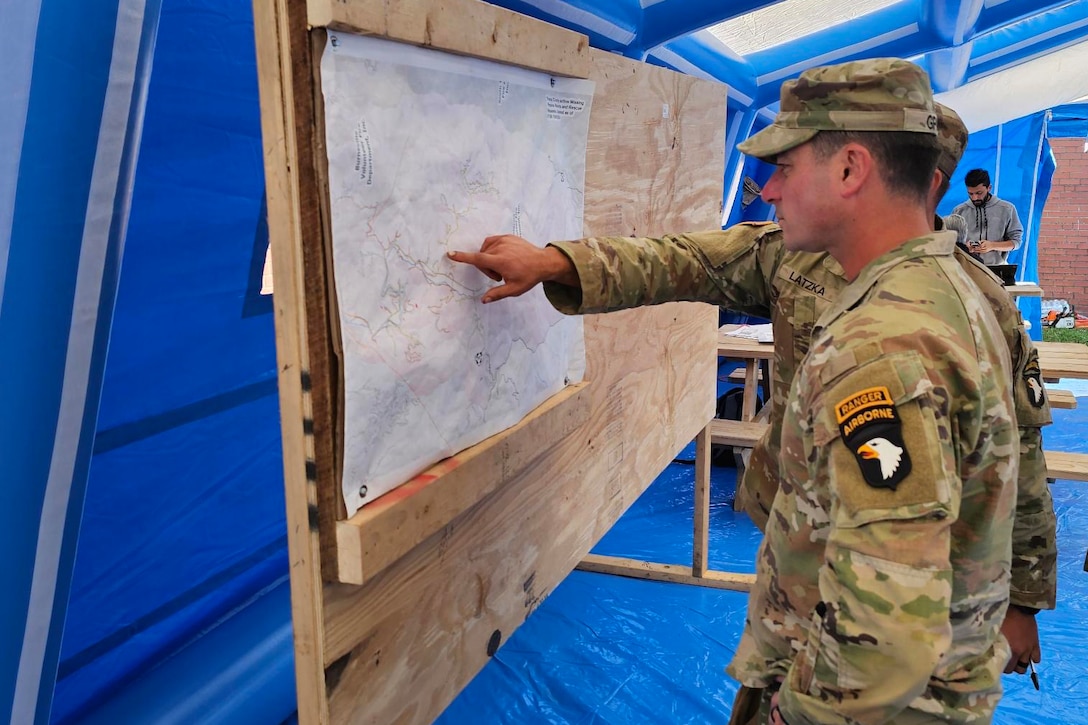 Soldiers look at a map on a board in a large, blue inflatable tent.