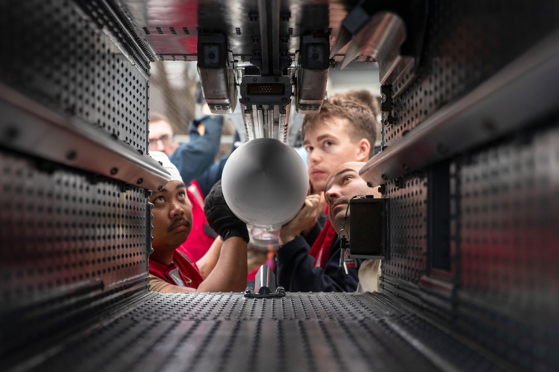 Four sailors load a missile into a square system.