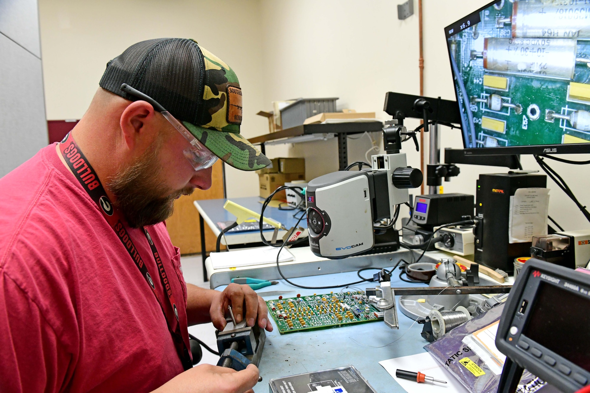 Man sits in front of a computer while working on a circuit board