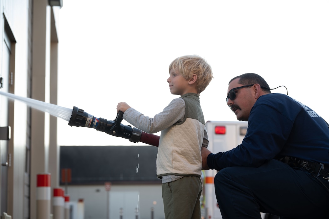 Terry Peck, 436th Civil Engineer Squadron firefighter, teaches a young Team Dover member to use a fire hose during an open house at Dover Air Force Base, Delaware, Oct. 10, 2024. The open house took place during Fire Prevention Week, a nationally observed week used to educate people on fire prevention. (U.S. Air Force Photo by Dieondiere Jefferies)