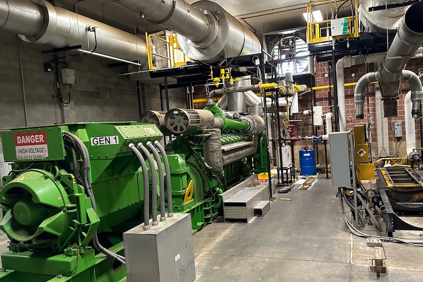 A large generator attached to many pipes sits in a large room.