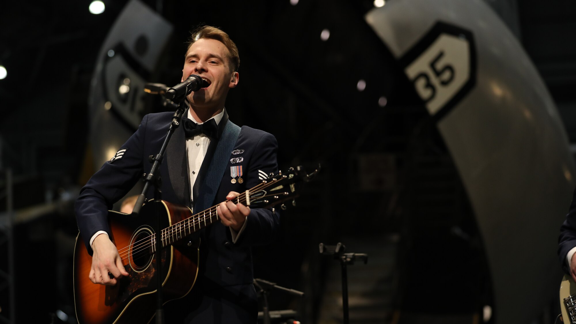Marik Chrisman playing an acoustic guitar and singing at a Flight One concert.