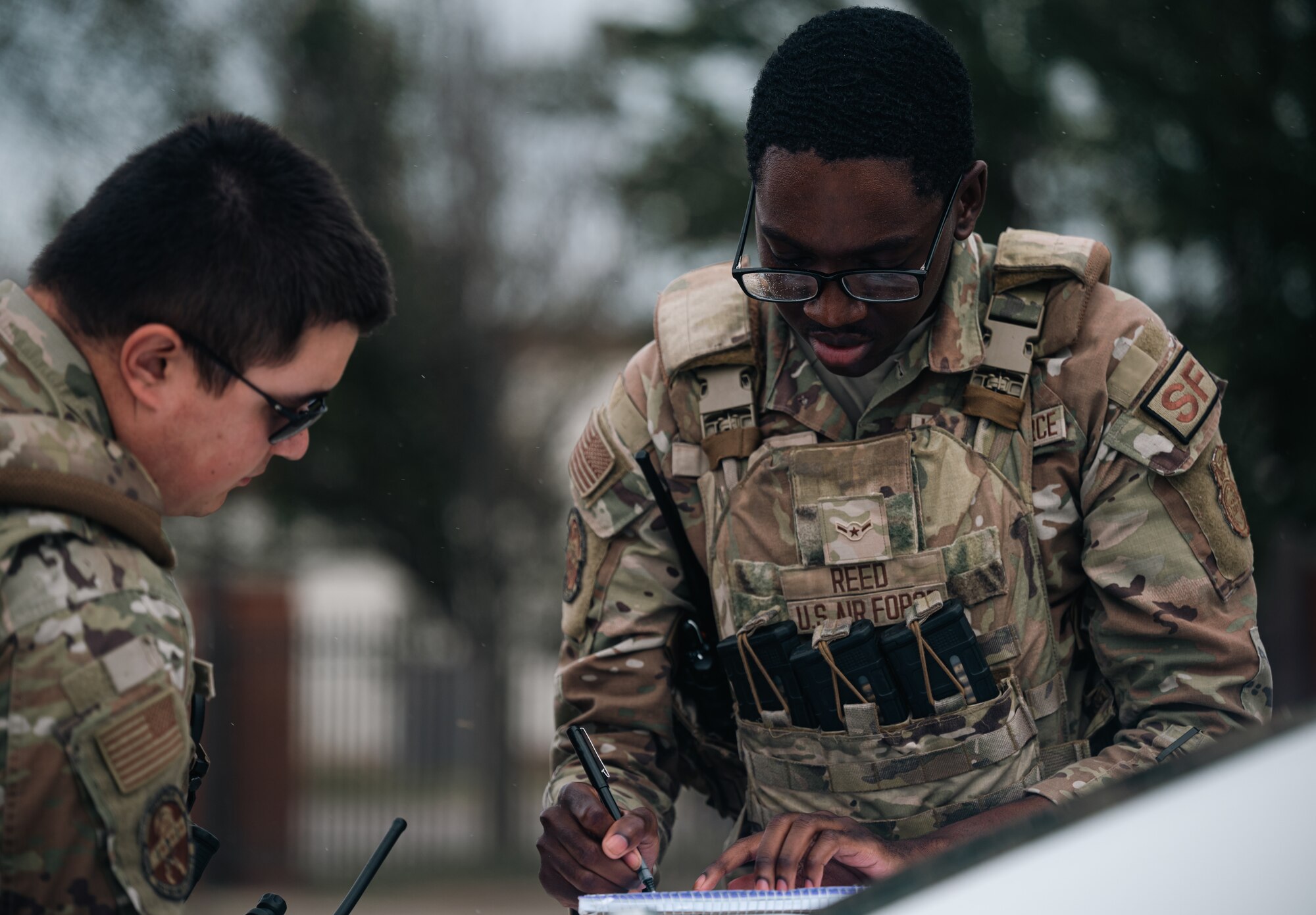 Airmen in uniforms lean over car with a note pad