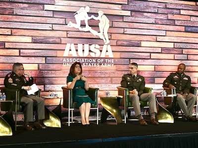 A woman on a panel speaks alongside three uniformed service members.