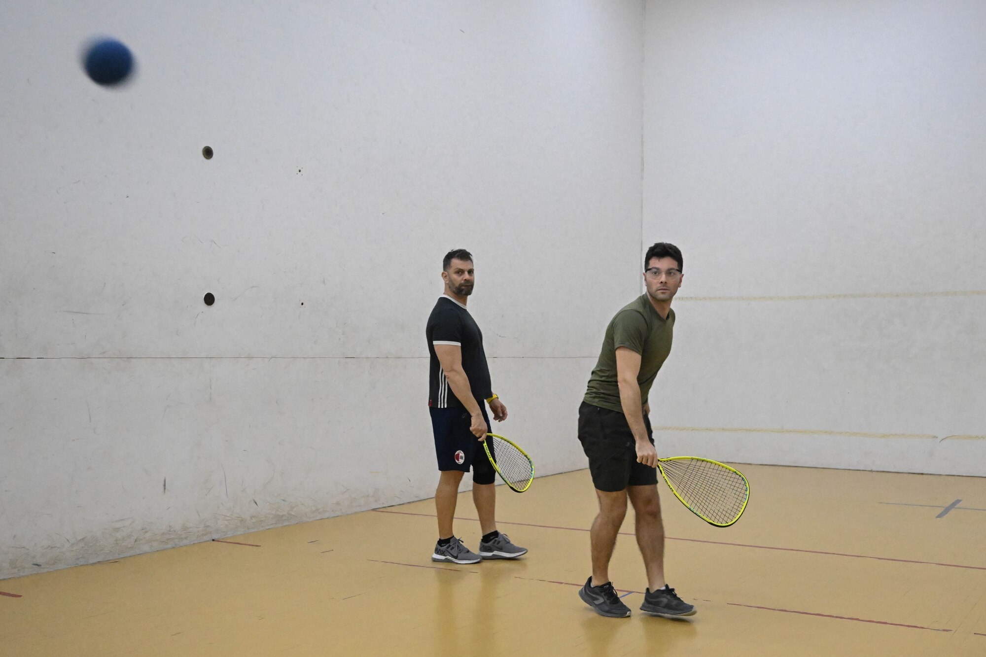 Two men watch a ball during a racquetball game.