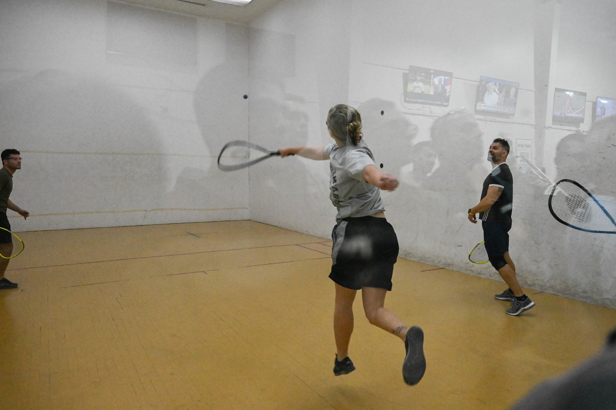 A woman jumps as she hits a ball during a racquetball match.