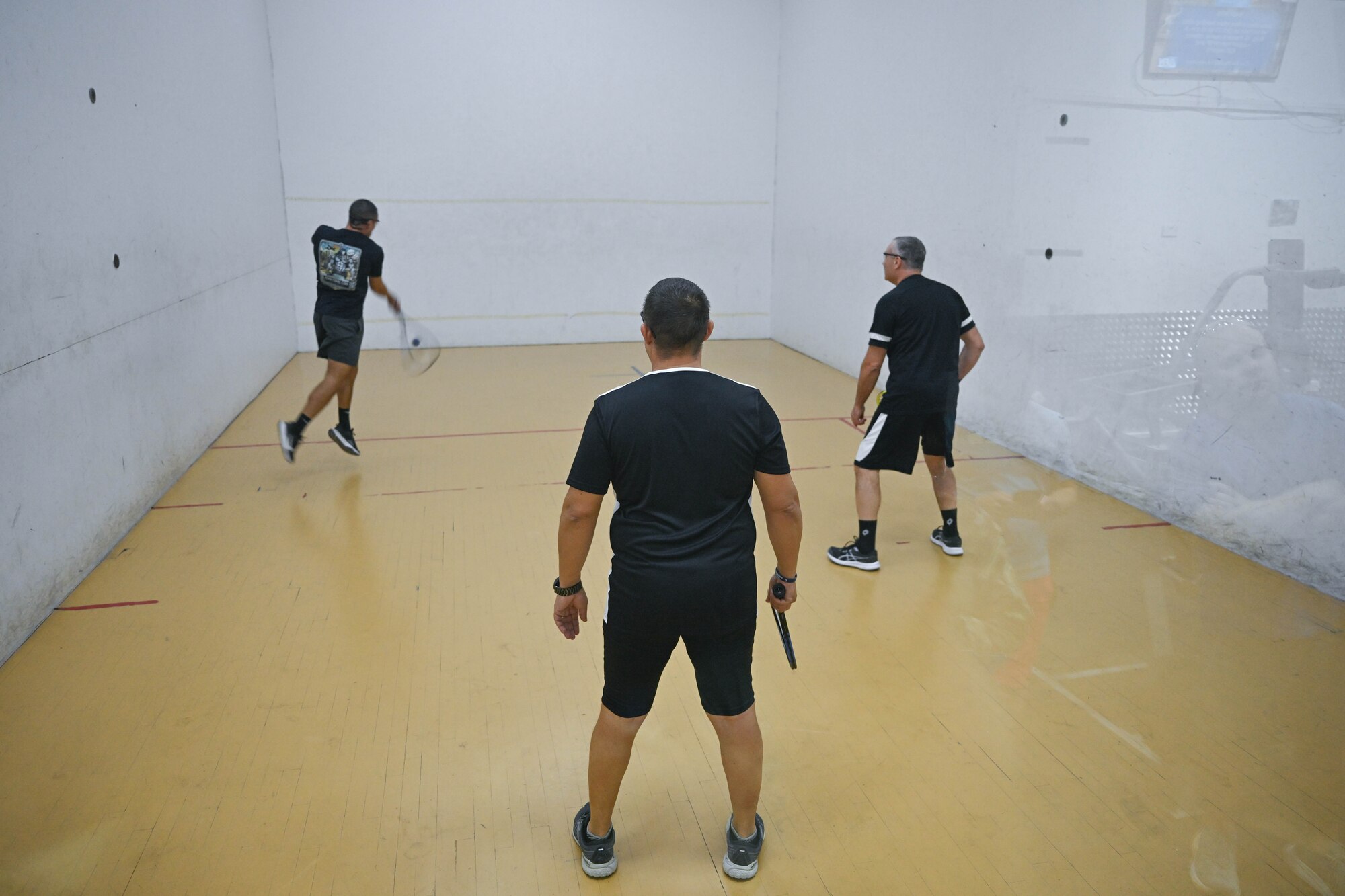 Three men play racquetball together.