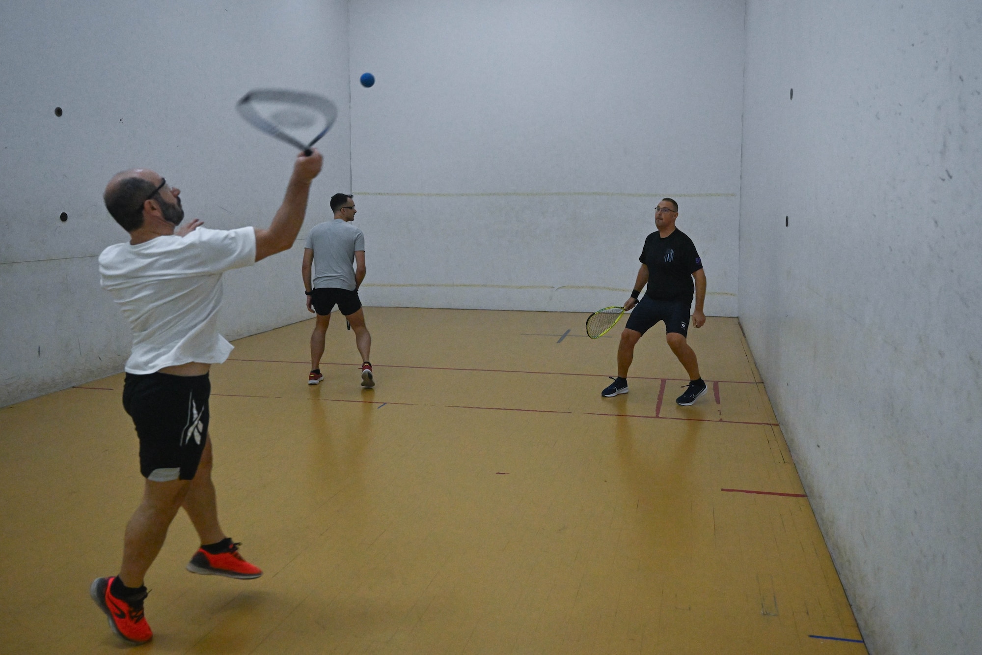 Three men play racquetball together.