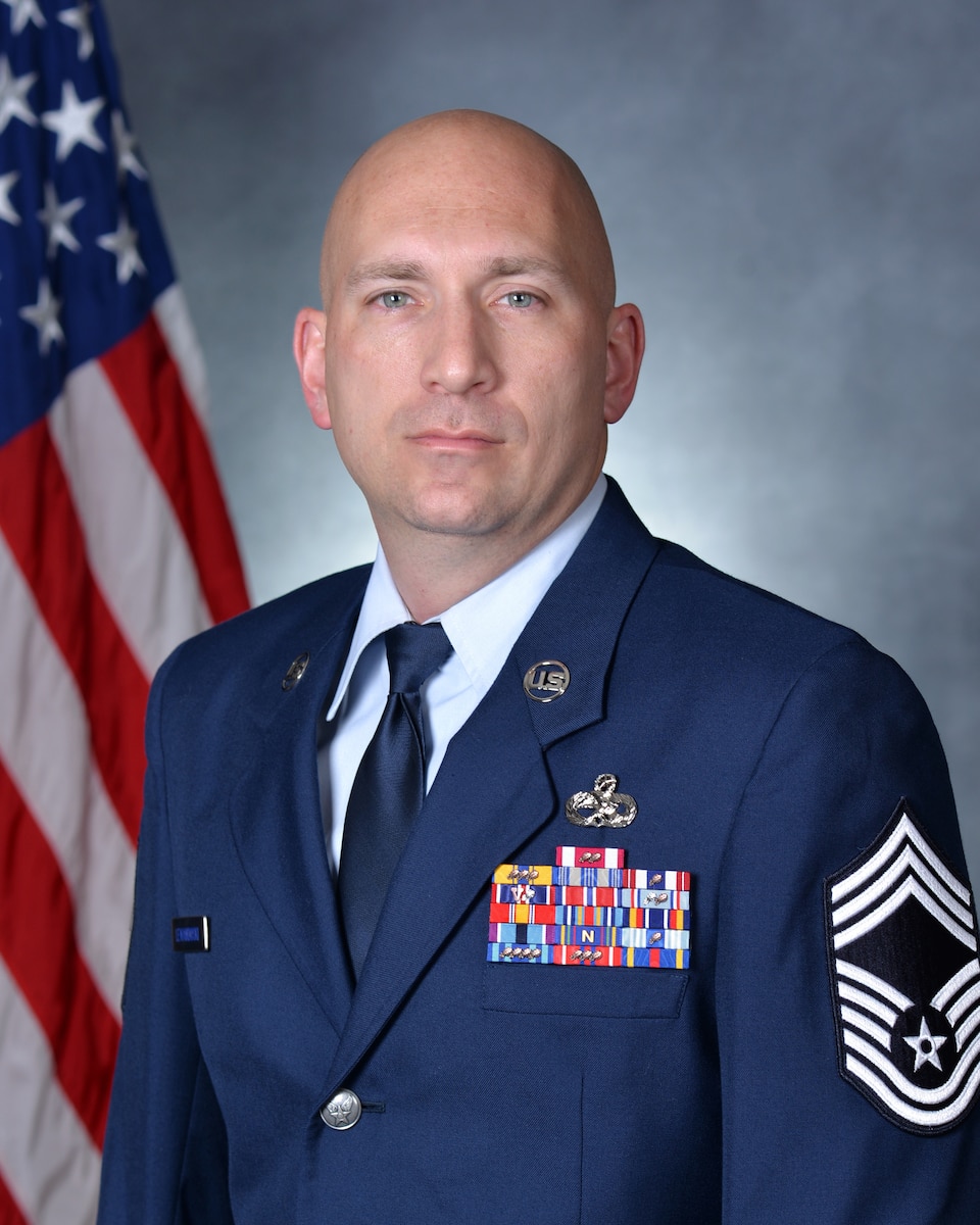 Man in dress blues posing for official photo in front of U.S. flag