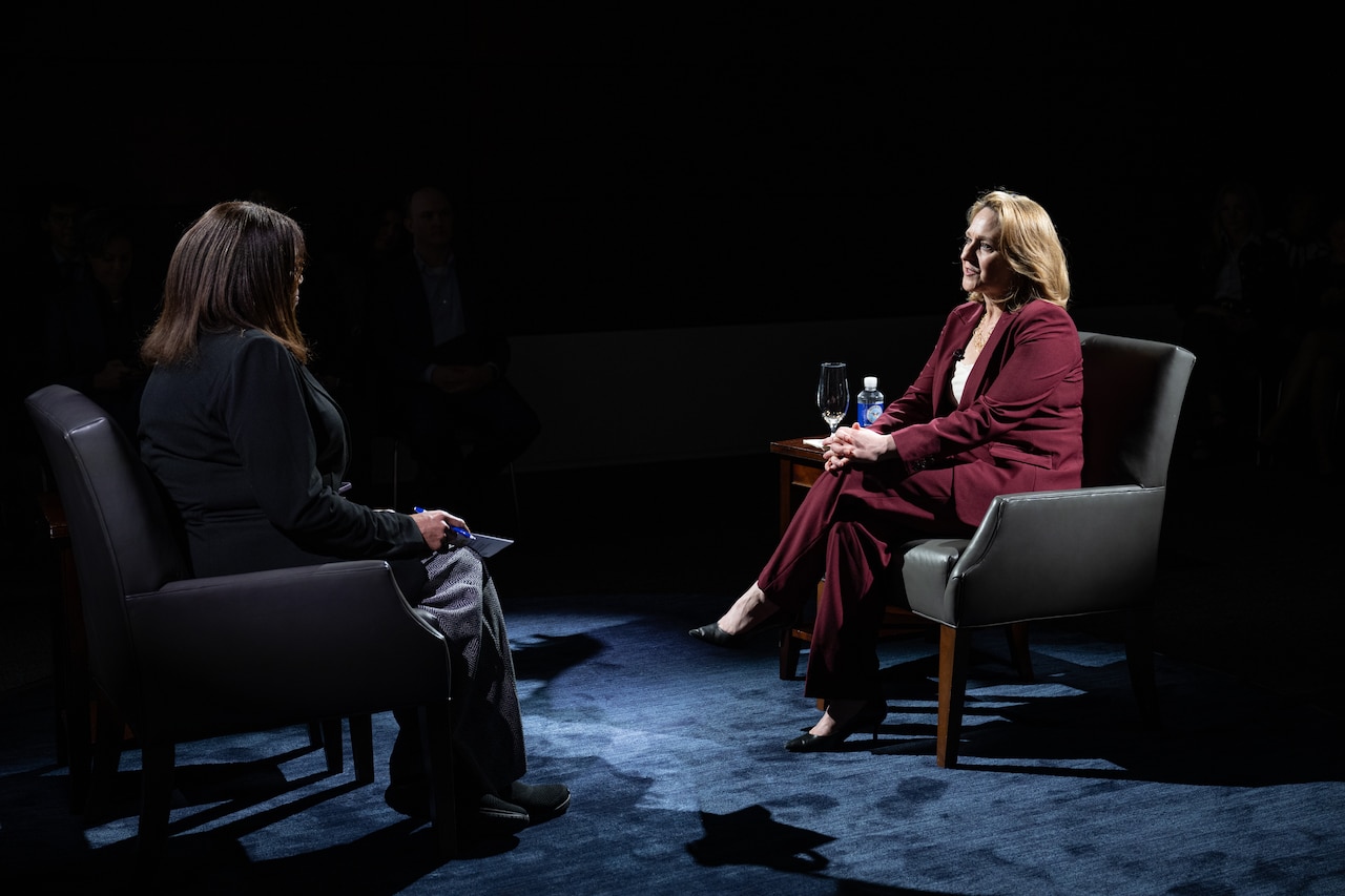 Two government officials sit on comfortable chairs across from one another and talk.