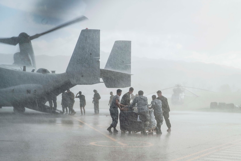 U.S. and Philippine troops move a pallet in the rain as fellow service members unload an aircraft in the background.