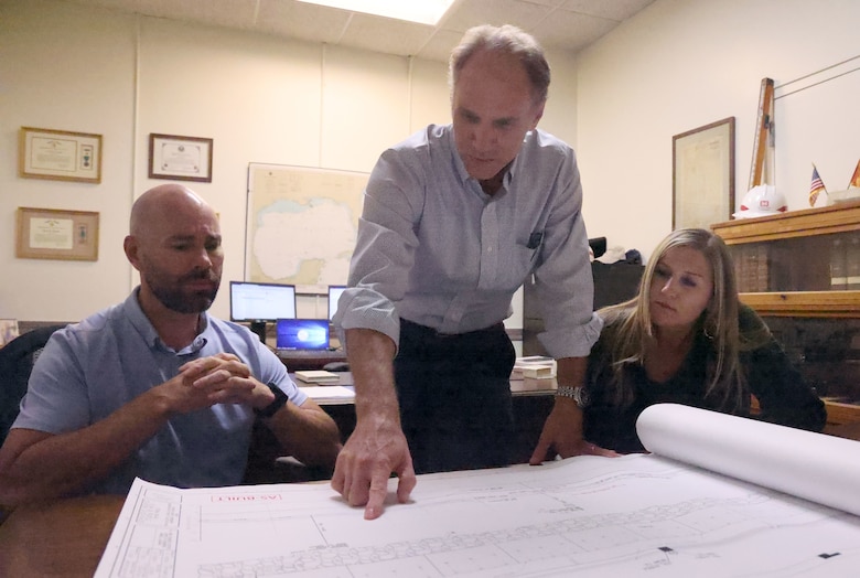 Two men and a woman lookin at a blueprint.
