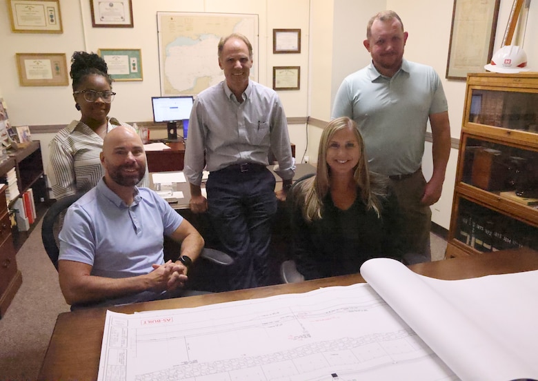 A group of people behind a desk looking at a blueprint.