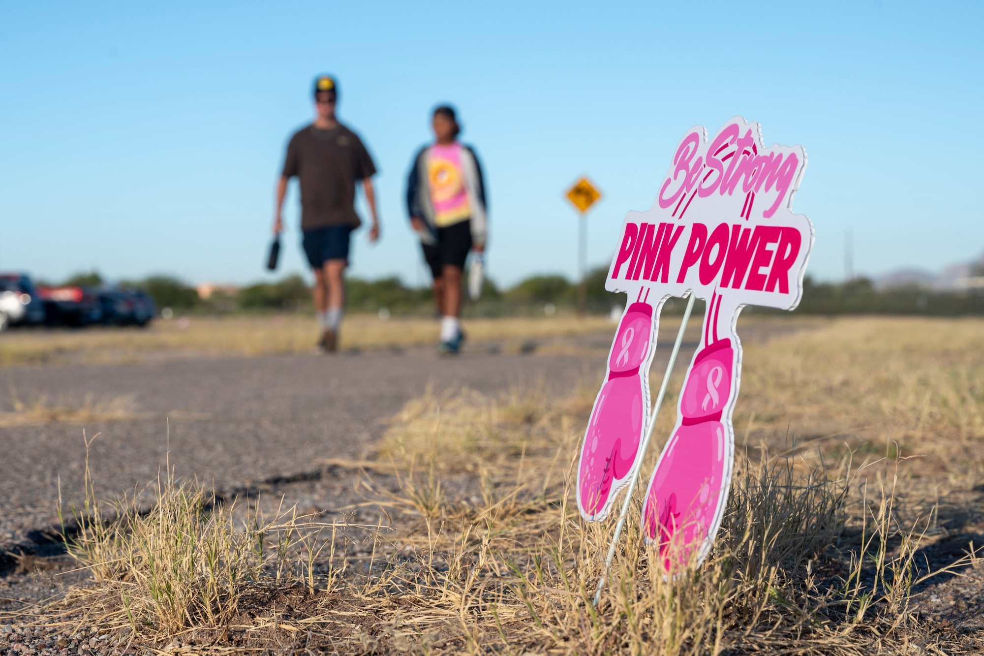 Two people walk together in the background as a breast cancer awareness sign fills the foreground.
