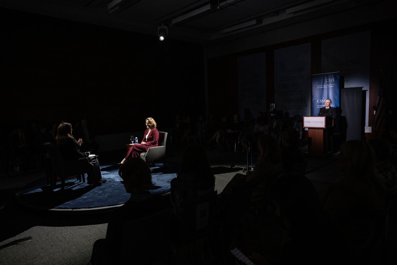 Two women sit on a darkened set.