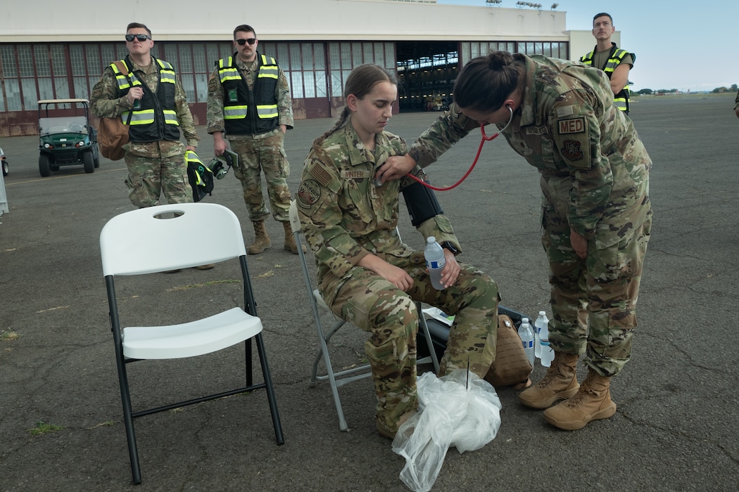 U.S. Air Force Maj. Christine Hargrave, a medical doctor with the 7th Expeditionary Airlift Squadron, checks Capt. Kaitlin Winter, a pilot assigned to the 7t EAS, for vitals and heart rate following decontamination procedures while Wing Inspection Team members observe in the background during Exercise Rainier War 25A, at Kalaeloa, Hawaii, Oct. 9, 2024.