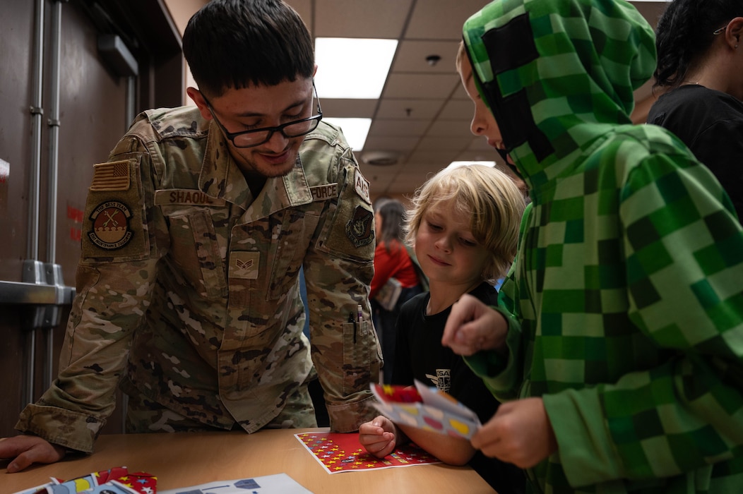 U.S. Air Force Senior Airman Jonathan Shaoul, 51st Maintenance Squadron avionics journeyman, assists children in making a paper airplane during an event at Osan Air Base, Republic of Korea, Oct. 15, 2024. The kids in aviation event had around 35 children ranging from ages 5-18 participating in various activities to learn more about aviation. (U.S. Air Force photo by Staff Sgt. Christopher Tam)